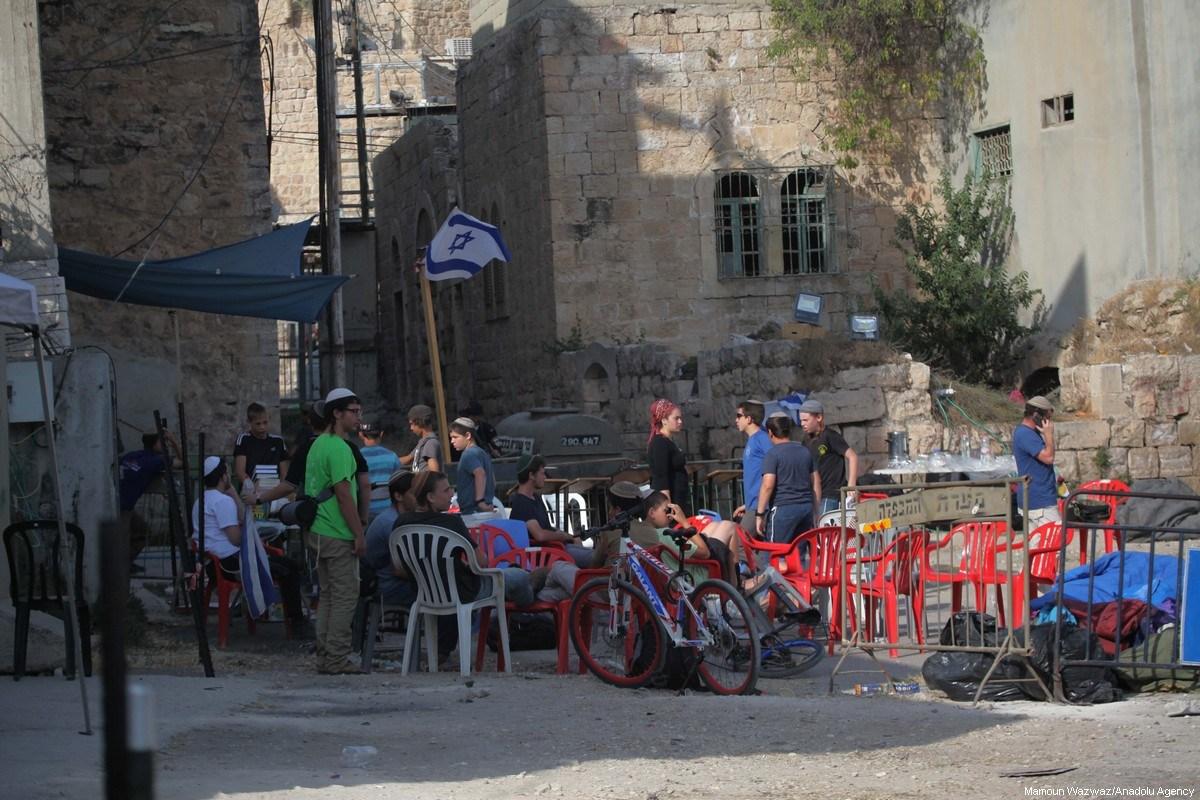 Colonos reúnem-se em frente à residência de uma família palestina, após despejarem seus proprietários legais e ocupá-la sob proteção israelense, em Hebron (Al-Khalil), Cisjordânia, 26 de julho de 2017 [Mamoun Wazwaz/Agência Anadolu]