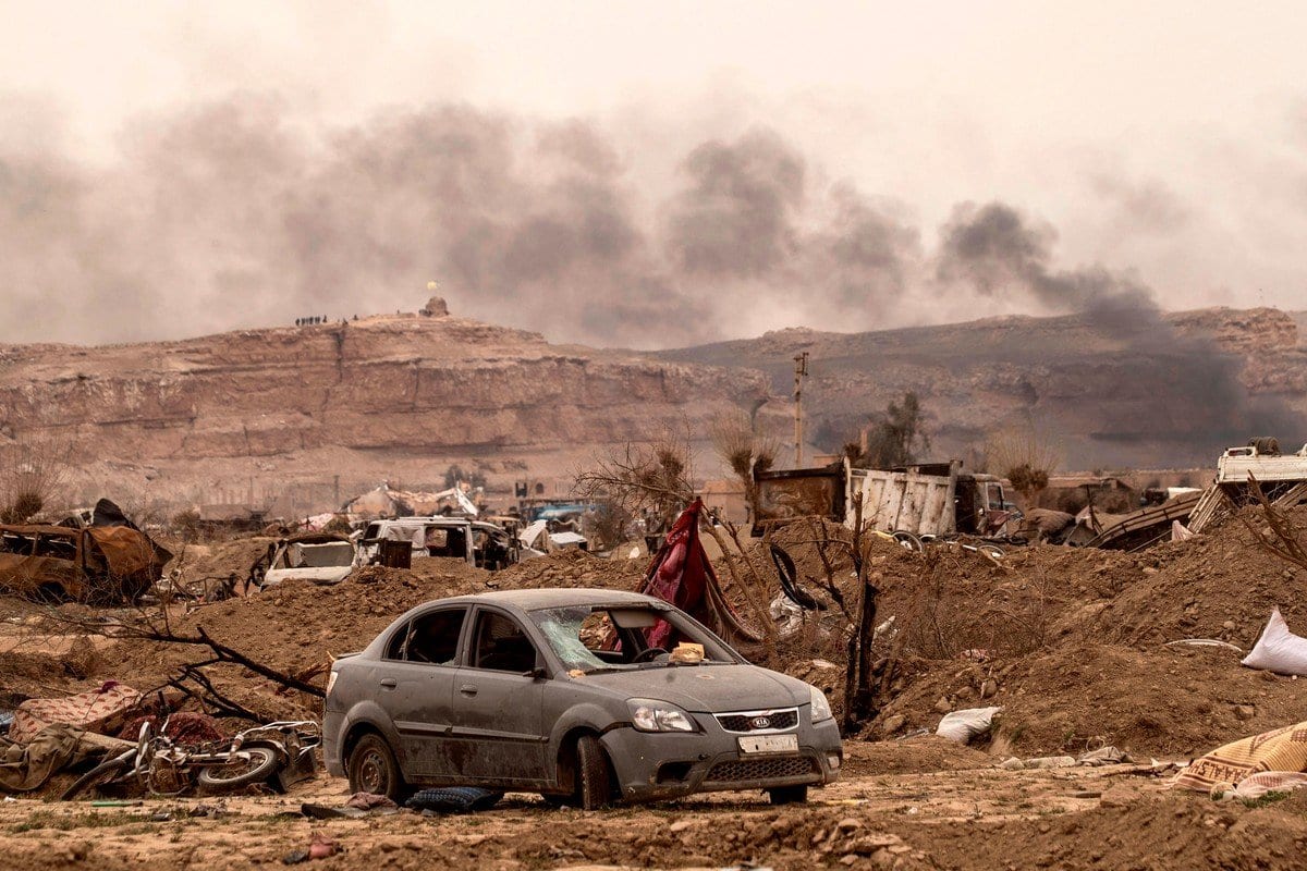 Veículos destruídos, destroços e fumaça ao fundo, na província de Deir Ezzor, leste da Síria, perto da fronteira iraquiana em 24 de março de 2019 24 de março de 2019 [Delil Souleiman/ AFP/ Getty Images]