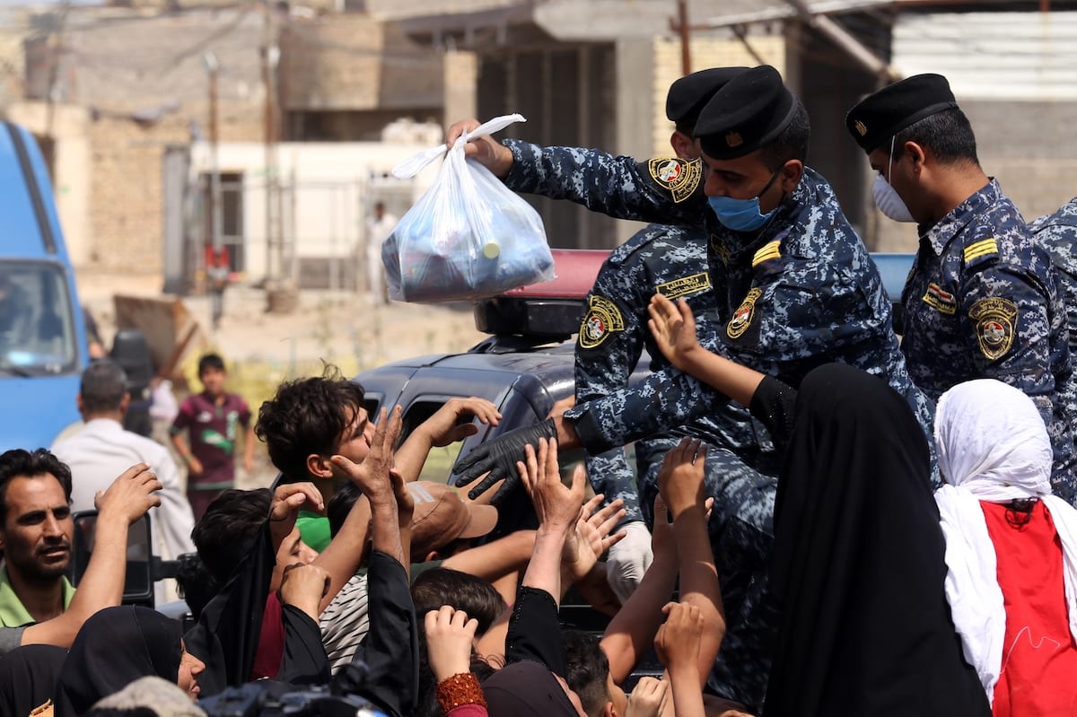 Forças de segurança iraquianas distribuem alimento para pessoas em necessidade durante a pandemia de coronavírus (covid-19), em Bagdá, capital do Iraque, 13 de abril de 2020 [Murtadha Al-Sudani/Agência Anadolu]