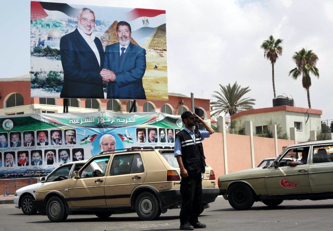 Um policial palestino, sob administração do Hamas, organiza o tráfego diante de uma fotografia do Presidente do Egito Mohammed Morsi ao lado do Primeiro-Ministro de Gaza Ismail Haniyeh, na Cidade de Gaza, em 29 de agosto de 2012 [Ashraf Amra/Apaimages]
