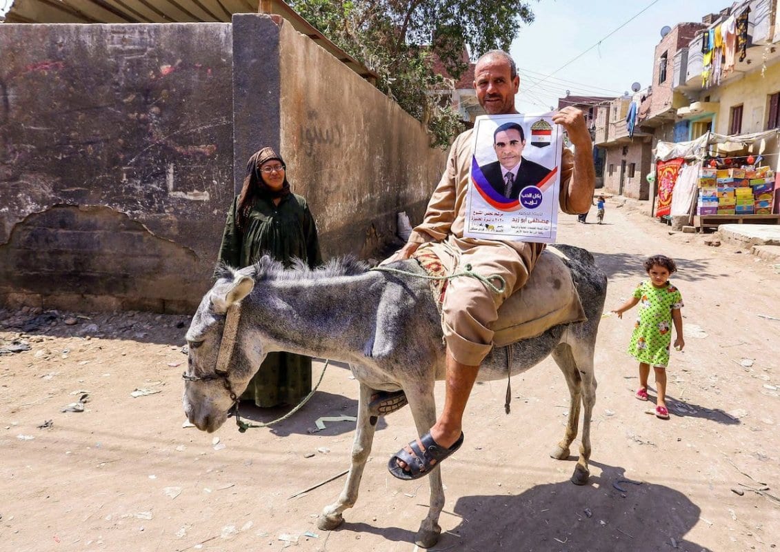 Homem montado em um burro exibe um cartaz de um candidato ao Senado, na aldeia de el-Ayyat, província de Giza, ao sul do Cairo, 11 de agosto de 2020 [AFP/Getty Images]