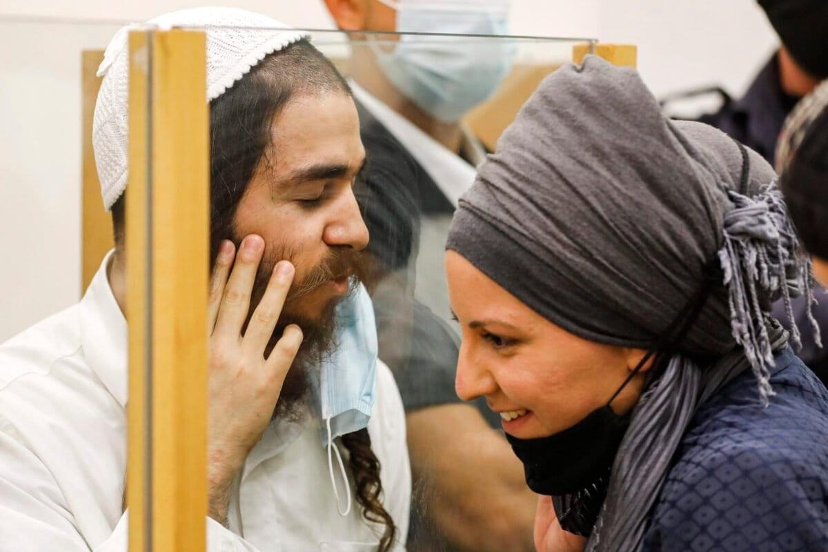 Amiram Ben-Uliel, extremista judeu condenado pelo incêndio criminoso de Duma, fala com sua esposa por trás de uma vidraça durante audiência de sentença, no tribunal distrital da cidade de Lod, no centro de Israel, 9 de junho de 2020 [Menahem Kahana/AFP/Getty Images]
