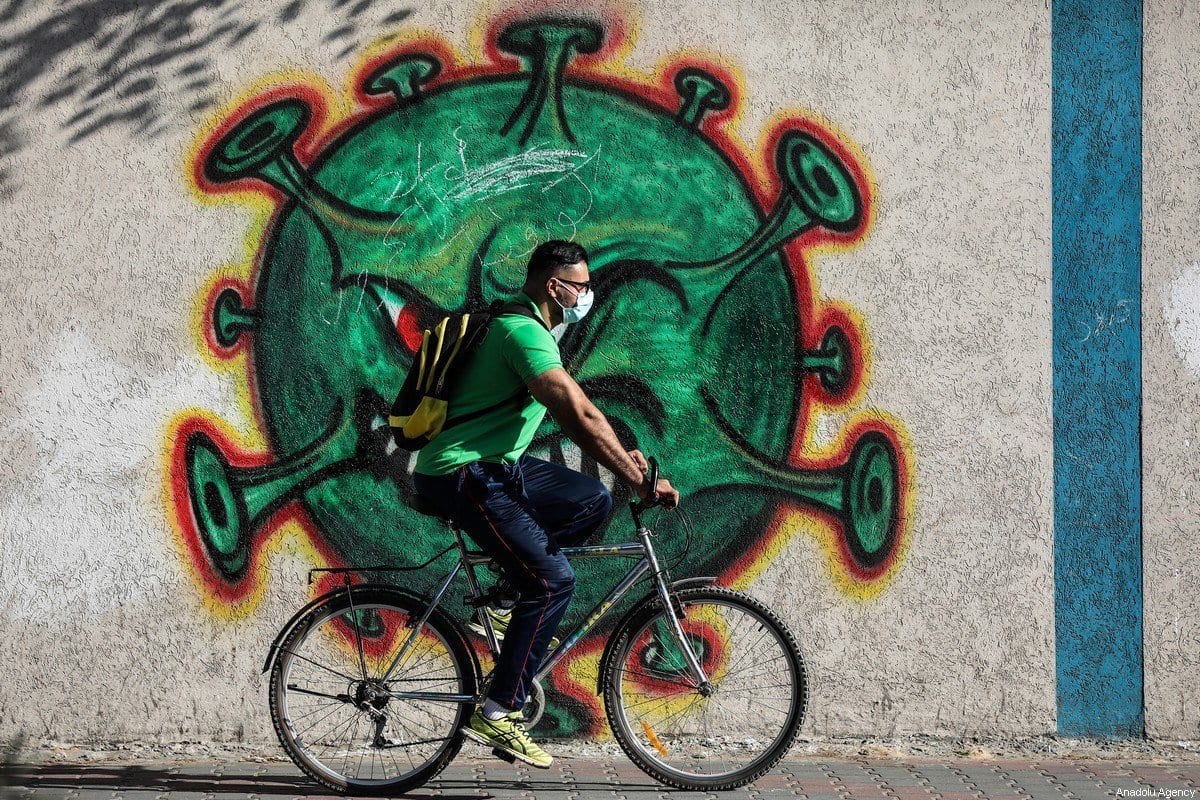 Homem usando máscara passa por um mural pintado com a figura de um vírus, em alerta de conscientização sobre a pandemia de covid-19, na Faixa de Gaza, 3 de outubro de 2020 [Mustafa Hassona/Agência Anadolu]
