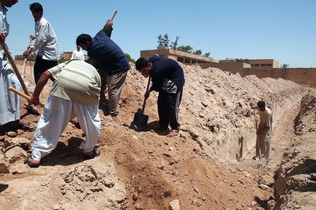 Iraquianos enterram um corpo em uma vala comum em um cemitério improvisado [Wathiq Khuzaie / Getty Image]