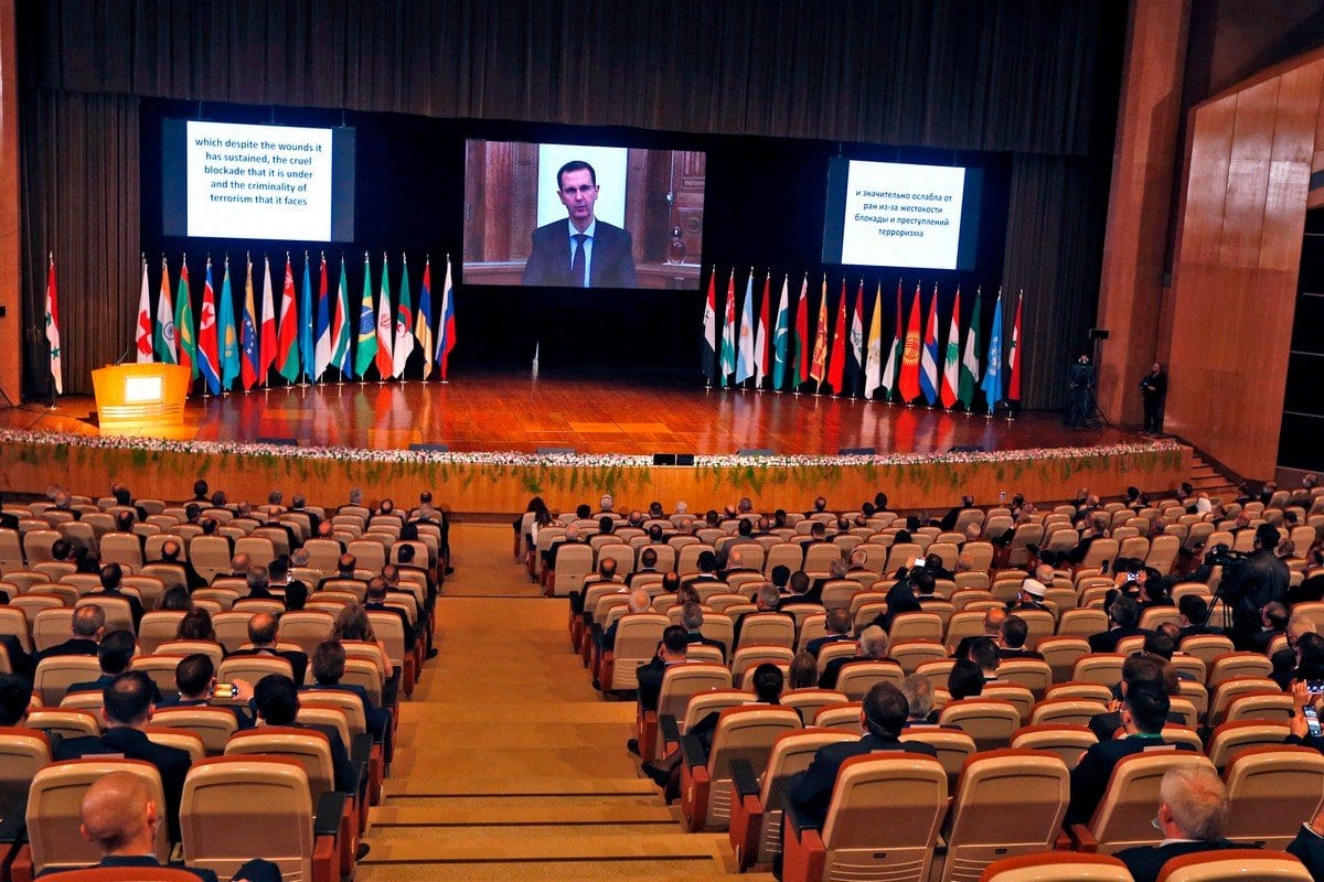 O presidente da Síria, Bashar Al-Assad (na tela) na conferência internacional sobre o retorno dos refugiados detidos em Damasco, em 11 de novembro de 2020 [Loual Beshara/ AFP / Getty Images]
