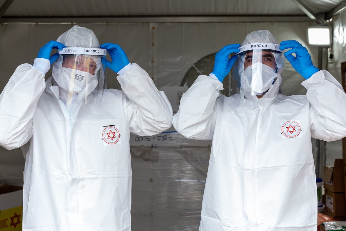Equipes médicas vestem roupas de proteção para conduzir testes de coronavírus em um posto móvel, em Tel Aviv, 1° de abril de 2020 [Guy Prives/Getty Images]
