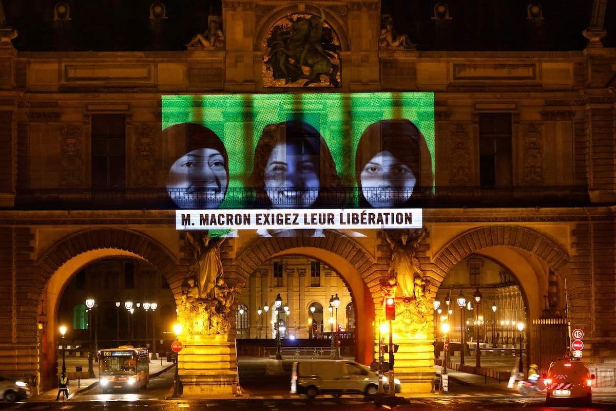Uma projeção no Museu do Louvre em Paris por membros da Anistia Internacional mostra imagens da ativistas sauditas de direitos humanos encarcerados, incluindo Loujain Al-Ahloul (centro), e a mensagem escrita: "Sr. Macron, exija sua libertação", antes do lançamento virtual Cúpula do G20, em 19 de novembro de 2020 [Thomas Coex/ AFP via Getty Images]