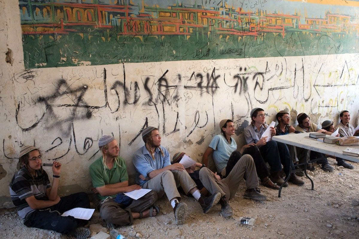 Colonos israelenses sentam-se no antigo assentamento Sanur no norte da Cisjordânia, que foi evacuado por Israel em 2005, depois que cerca de 200 colonos entraram ilegalmente no local, em 28 de julho de 2015. [Menahem Kahana/ AFP via Getty Images] 
