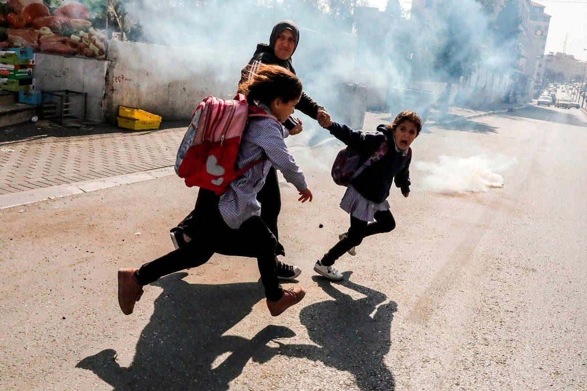 Uma mulher e duas meninas em idade escolar fogem de gás lacrimogêneo disparado por forças israelenses na Cisjordânia ocupada, 17 de novembro de 2019 [Hazem Bader/AFP/Getty Images]