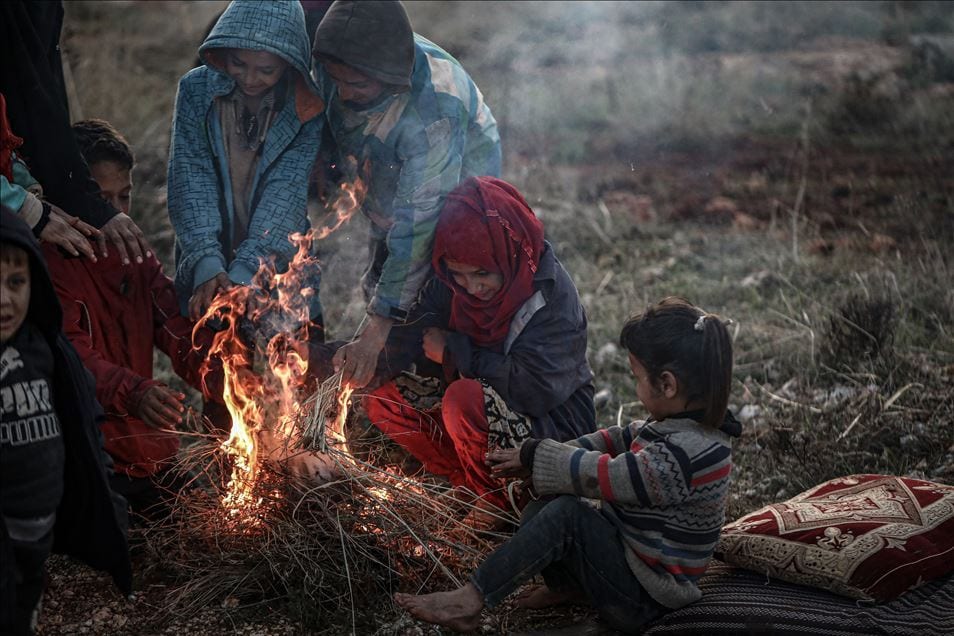 Crianças refugiadas sírias se amontoam em torno de uma fogueira para se aquecer em Idlib, Síria, em 28 de dezembro de 2019 [Muhammed Said / Anadolu Agency]

