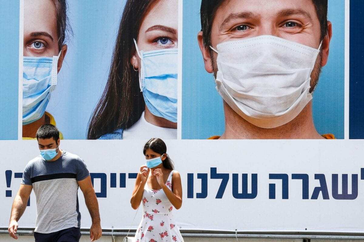 Cidadãos de máscara em frente a um outdoor promovendo medidas preventivas contra o covid-19, no centro da cidade israelense de Ramat Gan, leste de Tel Aviv, 17 de julho de 2020 [Jack Guez/AFP/Getty Images]