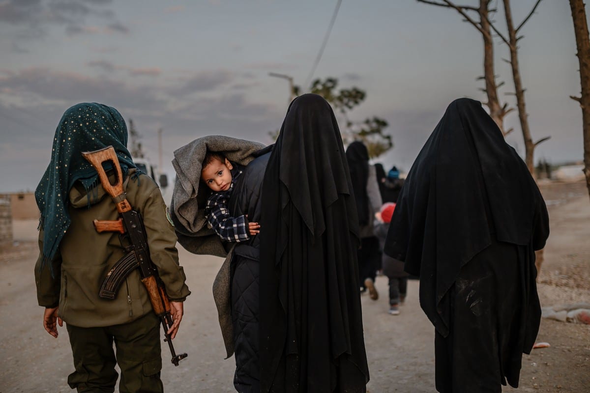 Mulheres sírias caminham sob escolta de uma combatente das Forças Democráticas Sírias (FDS) no campo de refugiados de Al-Hol, na Síria, em 17 de fevereiro de 2019 [Bulent Kilic/AFP/Getty Images]
