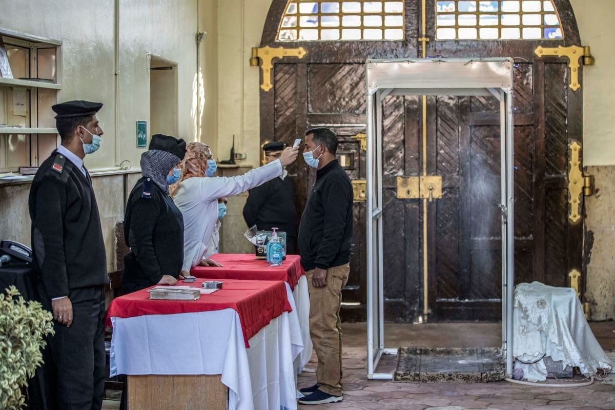 Mulher mede a temperatura corporal de um visitante na prisão feminina de al-Qanatir, em 27 de novembro de 2020. [Khaled Desouki/AFP via Getty Images]