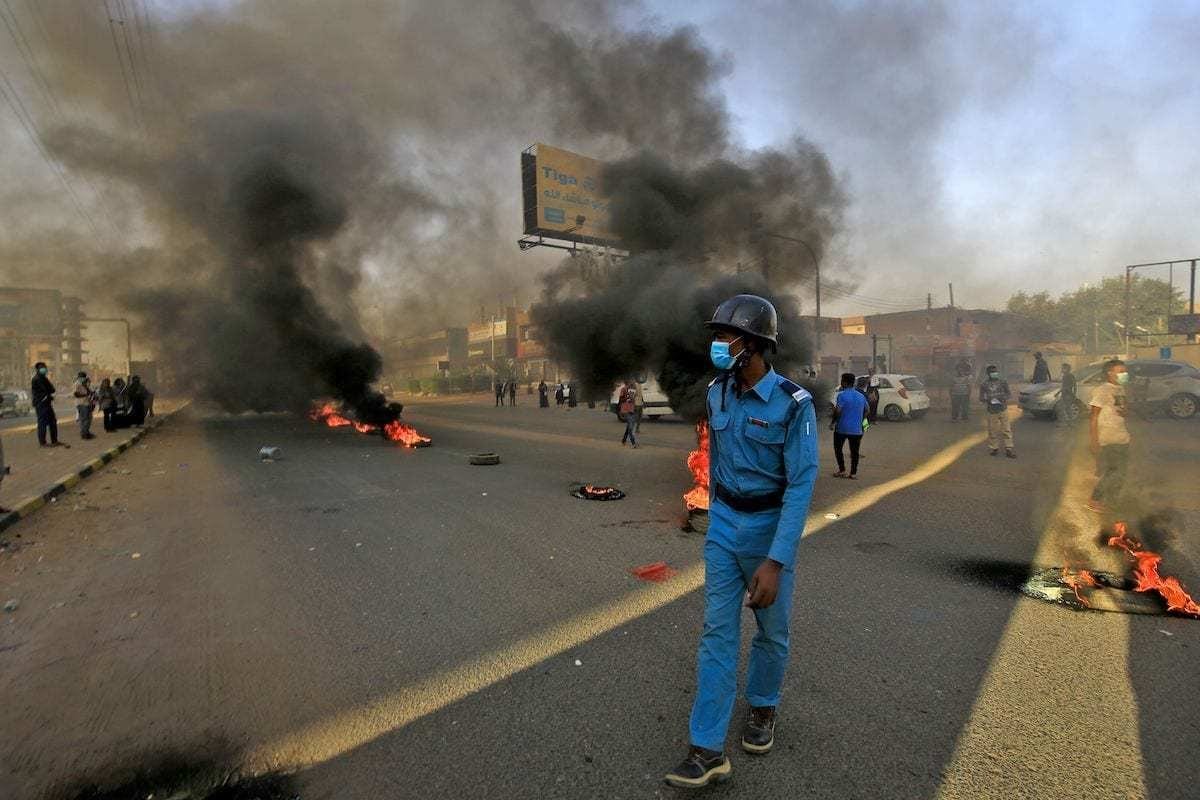 Policial passa perto de pneus incendiados por um protesto sudanês no primeiro aniversário da forte repressão contra um ato sit-in antigoverno, no distrito de Riad, leste de Cartum, capital do Sudão, 3 de junho de 2020 [Ashraf Shazly/AFP via Getty Images]

