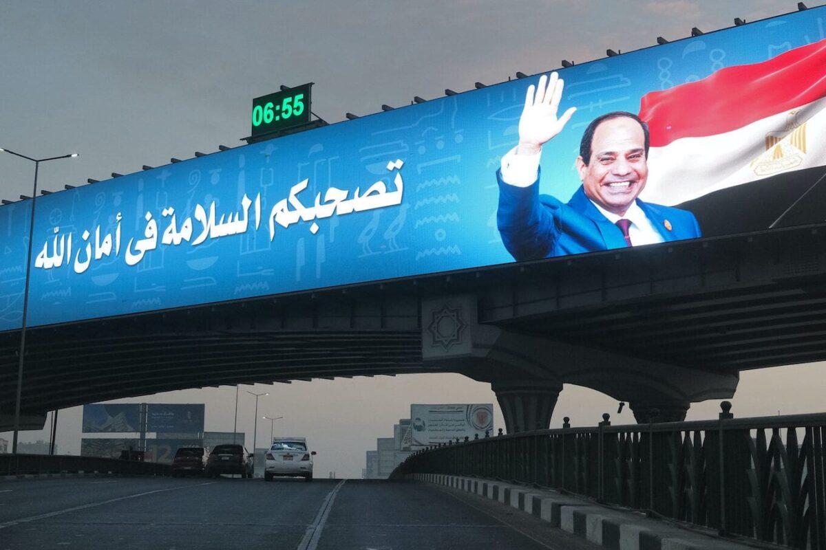 Outdoor eletrônico gigante no topo de uma ponte recentemente construída exibe o presidente Abdel Fattah al-Sisi ao lado de uma mensagem desejando viagens seguras aos motoristas que passam no distrito de Nasr City, capital do Egito, Cairo, em 15 de janeiro de 2021. [Amir Makar / AFP via Getty Images]
