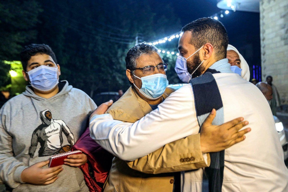 Mahmoud Hussein (C), um nacional egípcio e jornalista sênior da Al Jazeera árabe sediada no Catar, é abraçado por um homem ao chegar à casa de sua família na vila de Zawyet Abu Musallam em Gizé, cerca de 30 quilômetros ao sul da capital do Egito, Cairo, em 6 de fevereiro de 2021, após sua libertação da prisão. [AFP via Getty Images]
