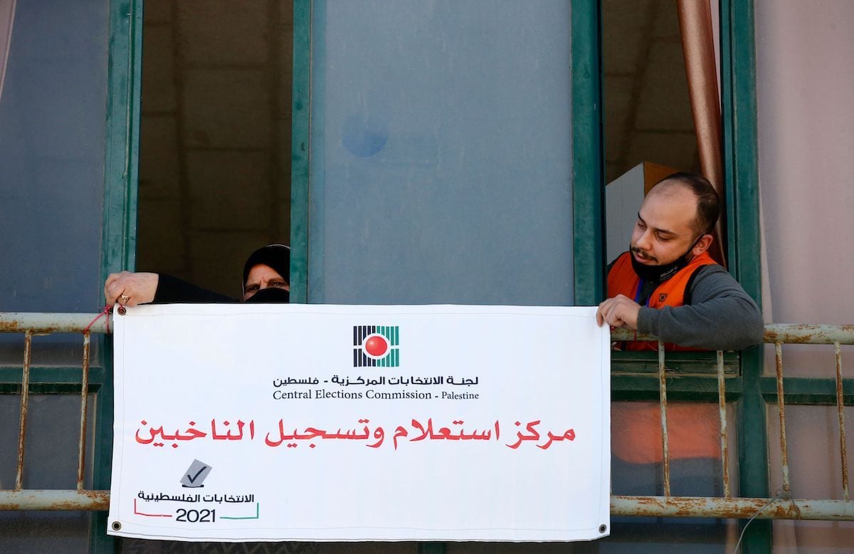 Membros da Comissão Eleitoral Central Palestina penduram uma placa em árabe onde se lê “centro de informações e registro de eleitores” na cidade de Hebron, na Cisjordânia, em 10 de fevereiro de 2021. [Hazem Bader/AFP via Getty Images]
