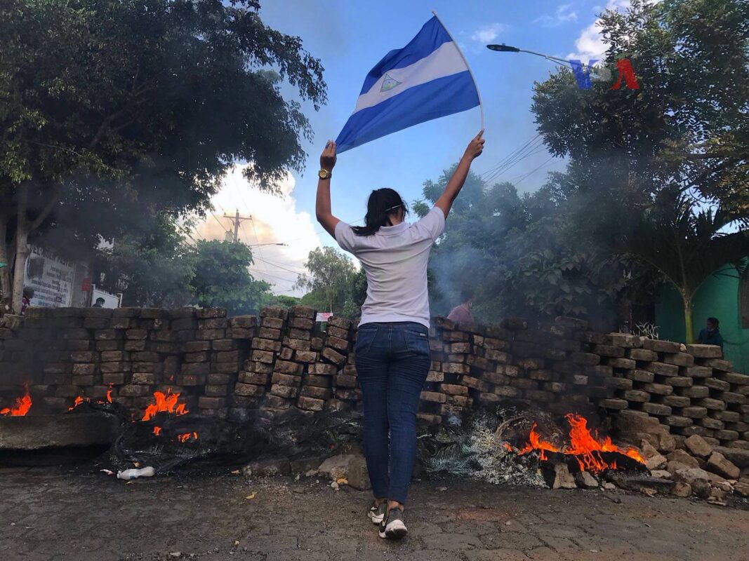  Uma mulher segurando a Bandeira da Nicarágua perto duma barricada em chamas. [Foto Wikipedia]