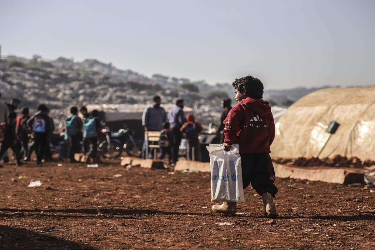 Criança carrega sacola plástica da Unicef para assistir aulas em uma escola improvisada no campo de refugiados de Reyyan, na aldeia de Kafr Uruq, em Idlib, Síria, 24 de novembro de 2020 [Muhammed Abdullah/Anadolu Agency]