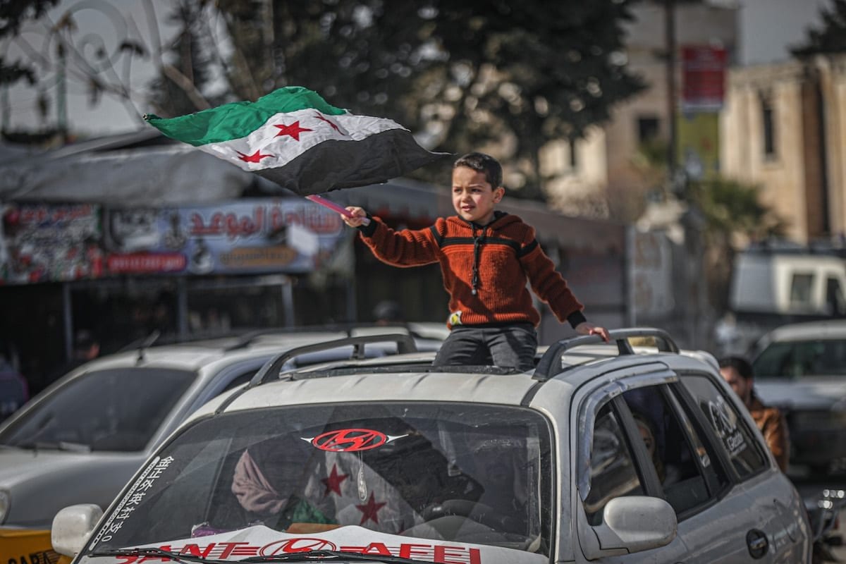 Civis sírios segurando estandartes e bandeiras, como o menino da foto, se reúnem para protestar pelo retorno à sua casa em Idlib , Síria em 19 de fevereiro de 2021. [Muhammed Said - Agência Anadolu]
