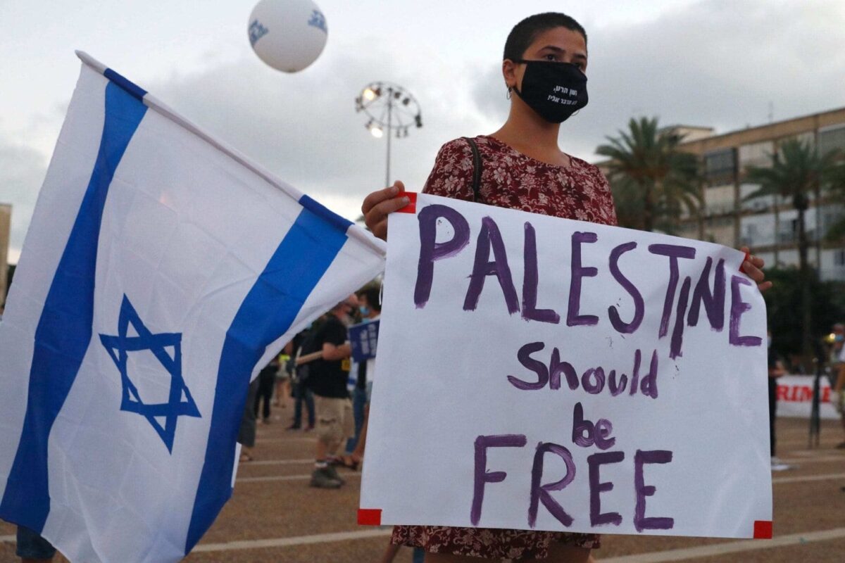 Um manifestante, usando uma máscara protetora devido à pandemia COVID-19, segura cartazes durante uma manifestação na Praça Rabin de Tel Aviv para denunciar o plano de Israel de anexar partes da Cisjordânia ocupada, em 23 de junho de 2020. [Jack Guez/ AFP via Getty Images]