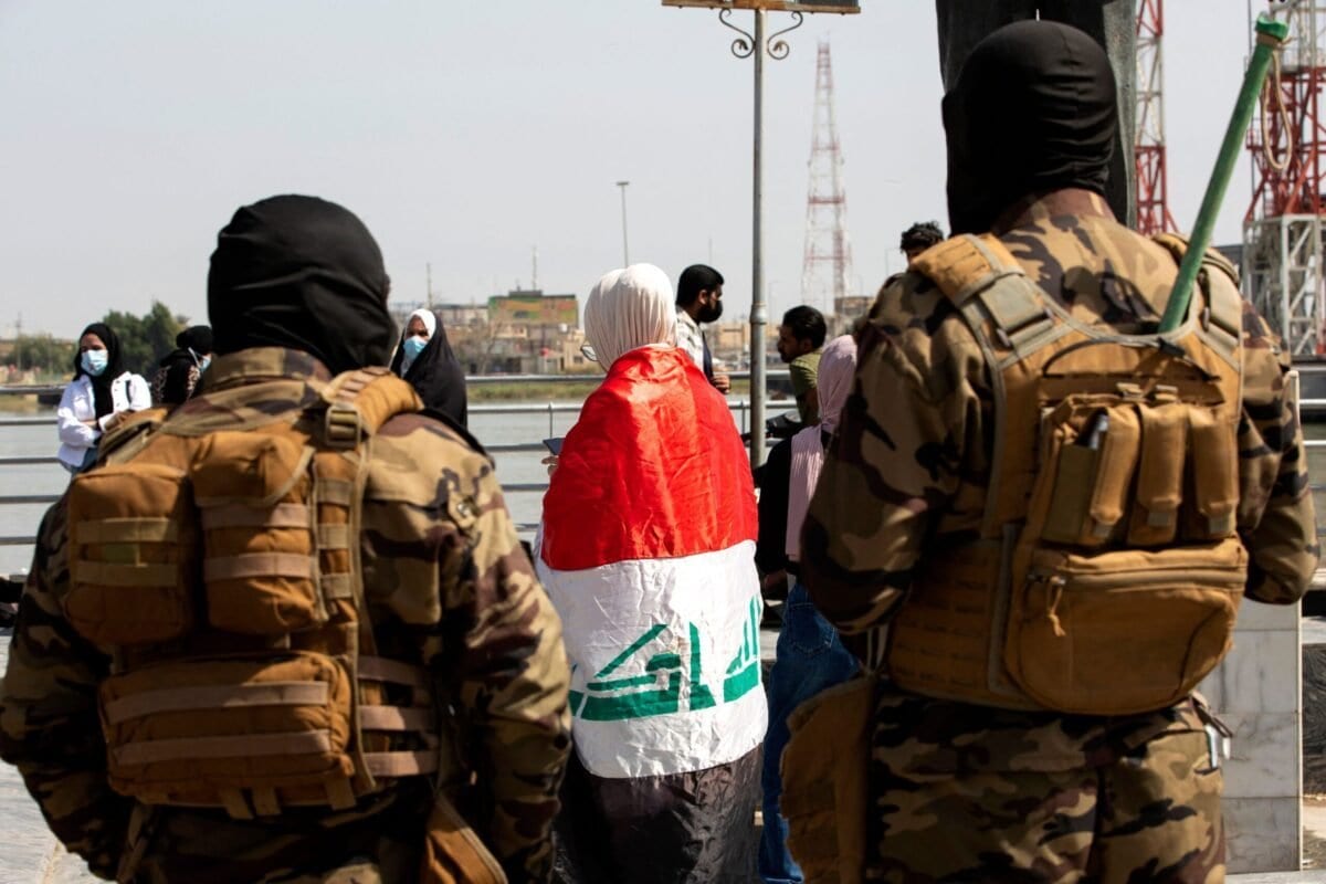 Forças de seguranças vigiam manifestantes envoltos na bandeira nacional, durante ato do Dia Internacional da Mulher, na cidade de Basra, sul do Iraque, 8 de março de 2021 [Hussein Faleh/AFP/Getty Images]
