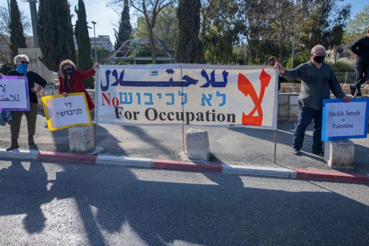 Ativistas palestinos, israelenses e estrangeiros erguem faixas e cartazes durante uma manifestação contra a ocupação israelense e atividades de assentamento nos Territórios Palestinos e em Jerusalém oriental, no bairro de Sheikh Jarrah palestino, em Jerusalém, em 19 de março de 2021. [Ahmad Gharabli/AFP via Getty Images]
