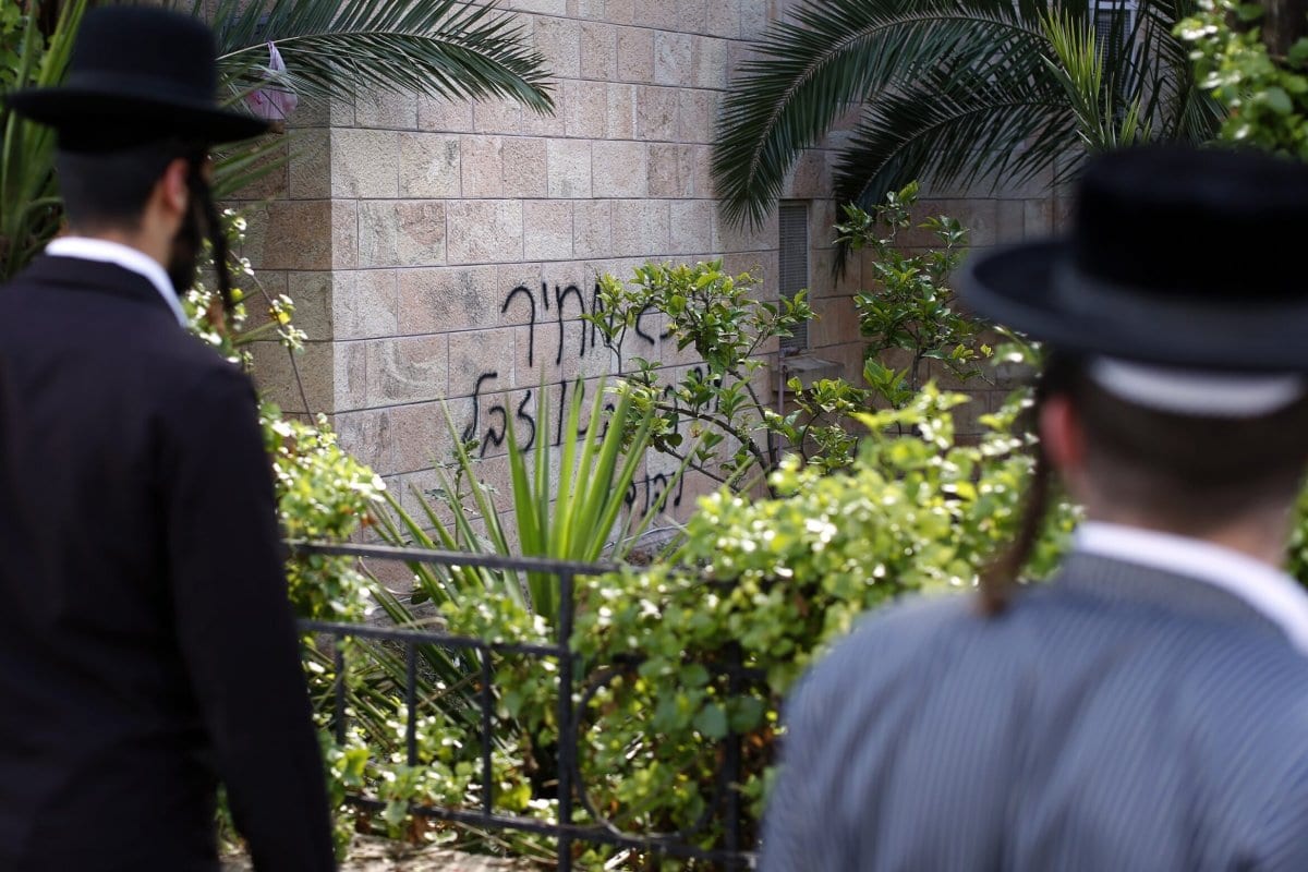 Dois judeus ultraortodoxos olham um grafite na parede de uma igreja que diz, em hebraico, “Rei David, rei dos judeus e Jesus é lixo, etiqueta de preço”, em 9 de maio de 2014 em Jerusalém. [Thomas Coex/AFP via Getty Images]
