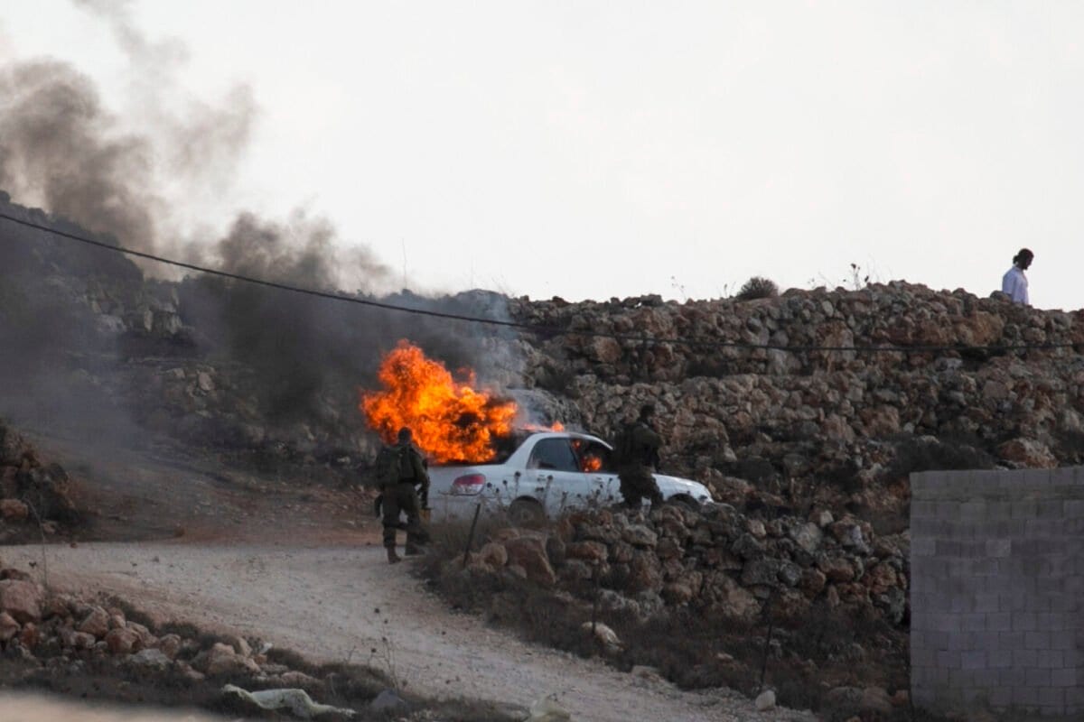Soldados israelenses passam por um carro em chamas na vila palestina de Qusra, na Cisjordânia ocupada, em 26 de setembro de 2020 [Jaafar Ashtiyeh/AFP via Getty Images]
