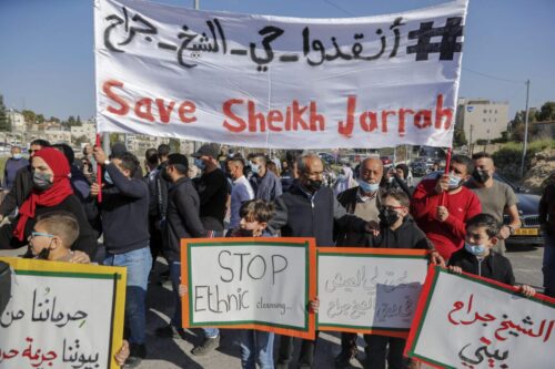 Ativistas palestinos, israelenses e estrangeiros exibem cartazes durante um protesto contra os assentamentos ilegais de Israel nos territórios palestinos ocupados, no bairro de Sheikh Jarrah, em Jerusalém, 19 de março de 2021 [Ahmad Gharabli/AFP/Getty Images]
