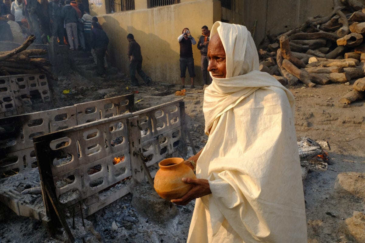 Monge hindu carrega uma tigela de água para derramar sobre as cinzas de um homem morto após a conclusão do ato de cremação em 28 de janeiro de 2018 [Kaveh Kazemi / Getty Images]
