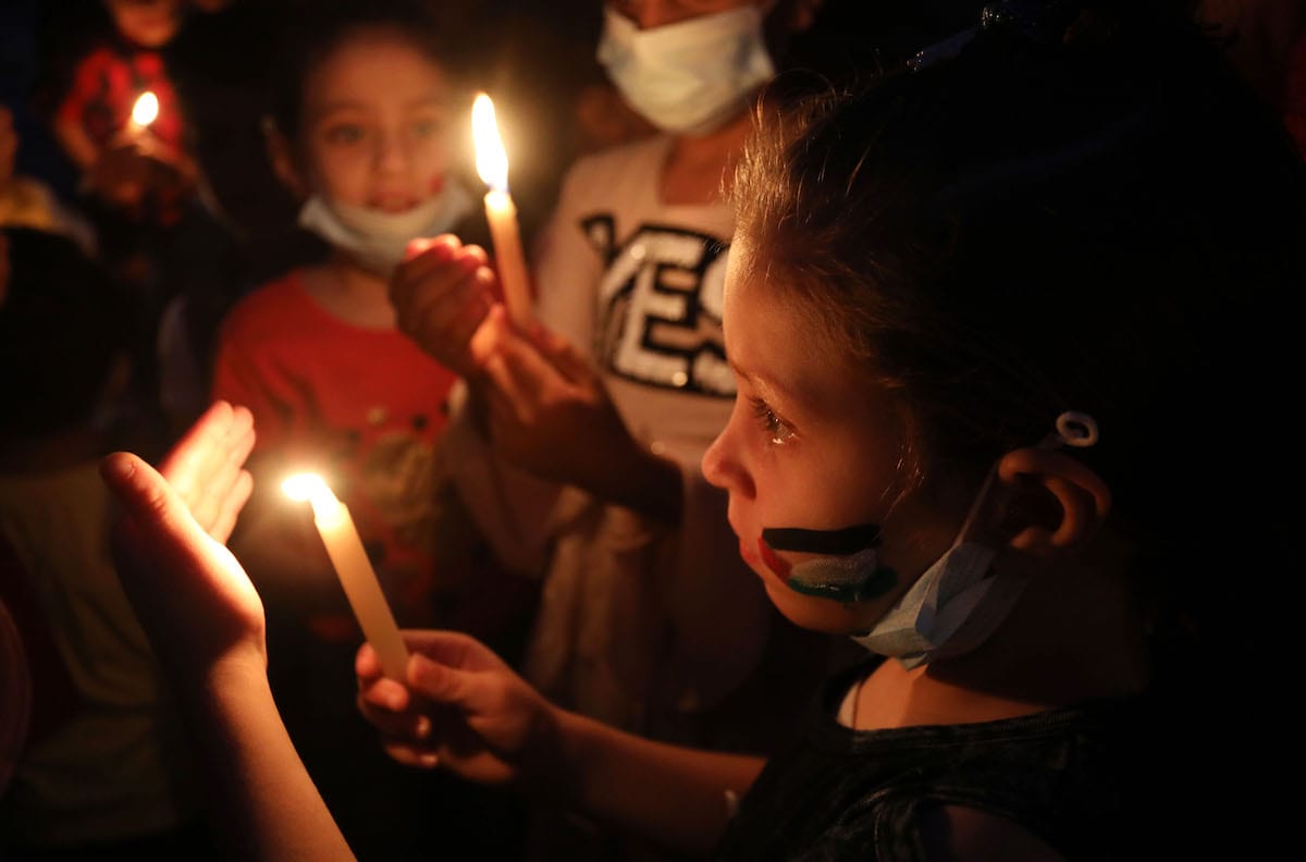 Crianças palestinas acendem velas em memória da família Abu Hattab, morta pelos ataques aéreos israelenses na Cidade de Gaza, 23 de maio de 2021 [Ashraf Amra/Agência Anadolu]
