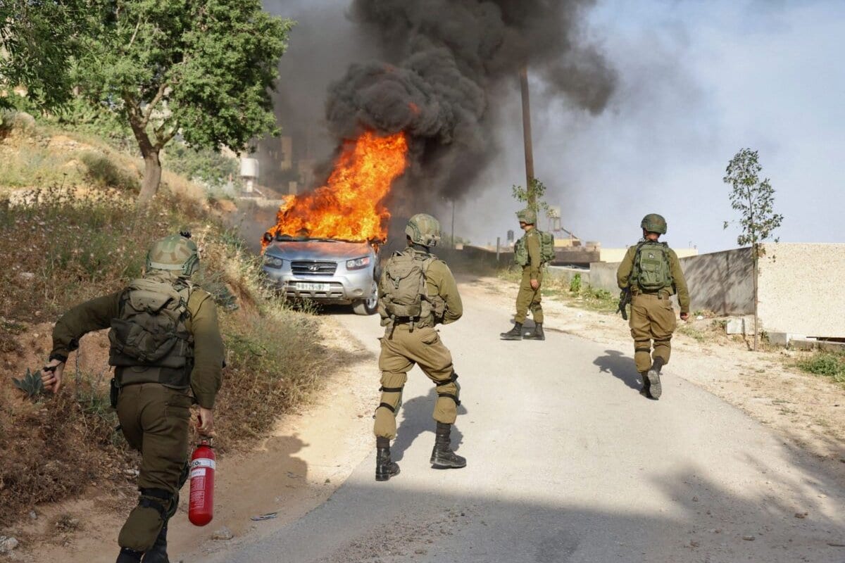 Um soldado israelense tenta extinguir as chamas de um veículo palestino em chamas durante uma operação de segurança na vila de Aqraba, a leste de Nablus, na Cisjordânia ocupada, em 3 de maio de 2021 [Jaafar Ashtiyeh/AFP via Getty Images]