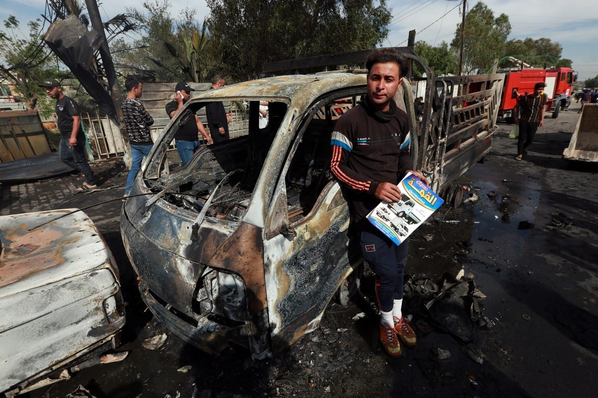 Pessoas vasculham os destroços de um veículo após um atentado a bomba que deixou um morto e catorze feridos, na área de al-Habibiya, na cidade de al-Sadr, a leste de Bagdá, Iraque, 15 de abril de 2021 [Murtadha Al-Sudani/Agência Anadolu]