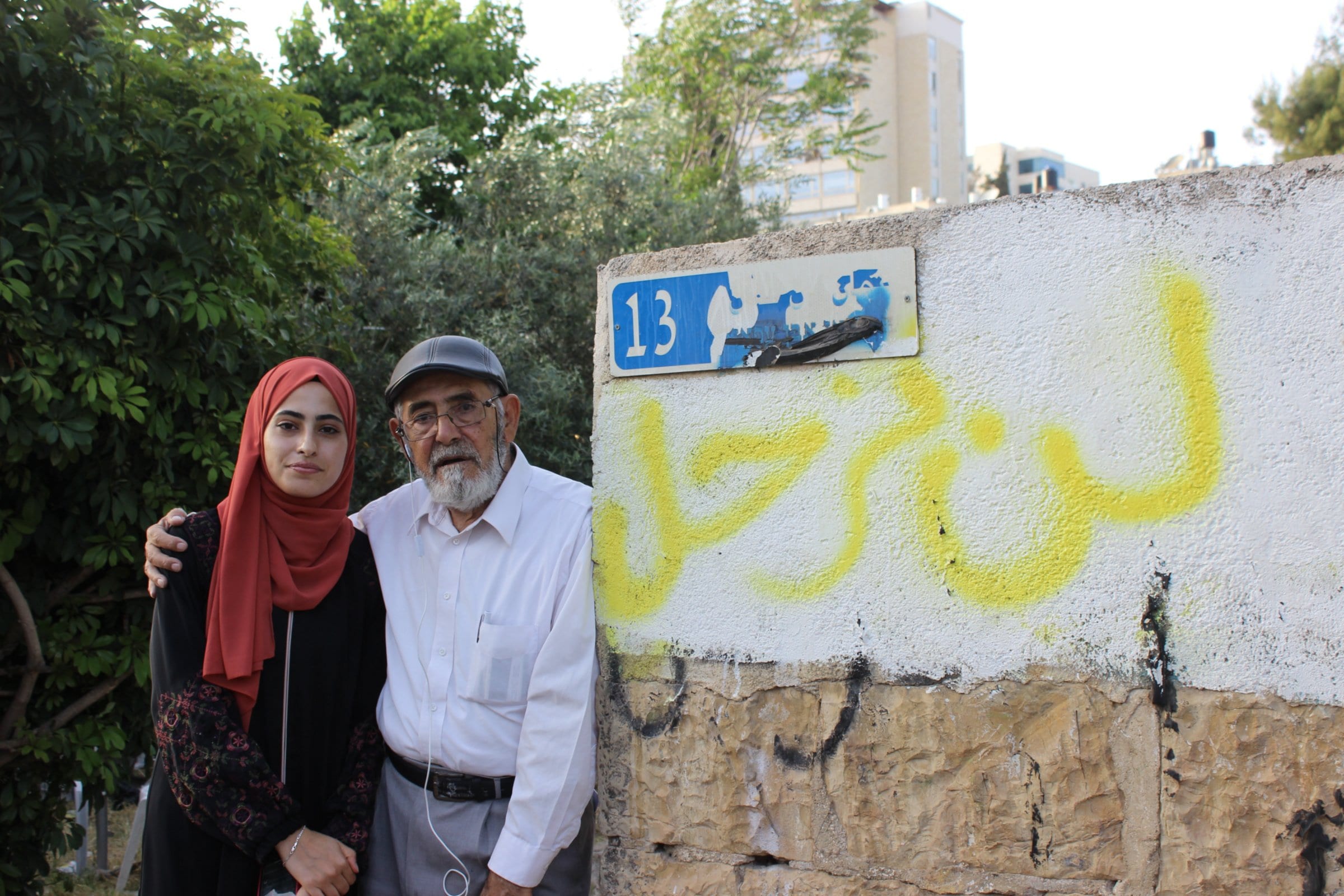 Muna e seu pai Nabil ao lado de um muro grafitado com a frase em árabe “Não sairemos” [Aseel al-Jundi/Middle East Eye]