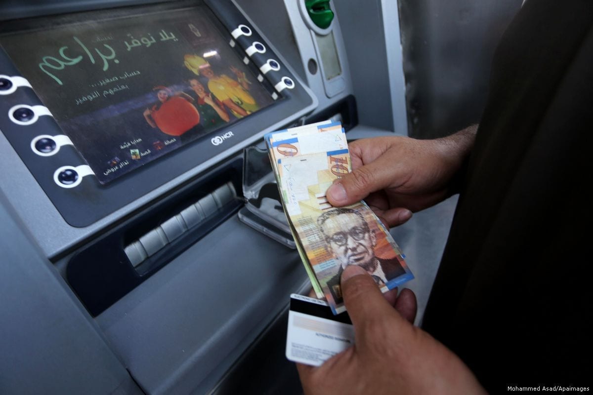 Palestinos, empregados pela Autoridade Palestina esperam para receber seus salários em um caixa eletrônico, em frente a um banco em Gaza, em 10 de maio de 2017 [Mohammed Asad/Apaimages]
