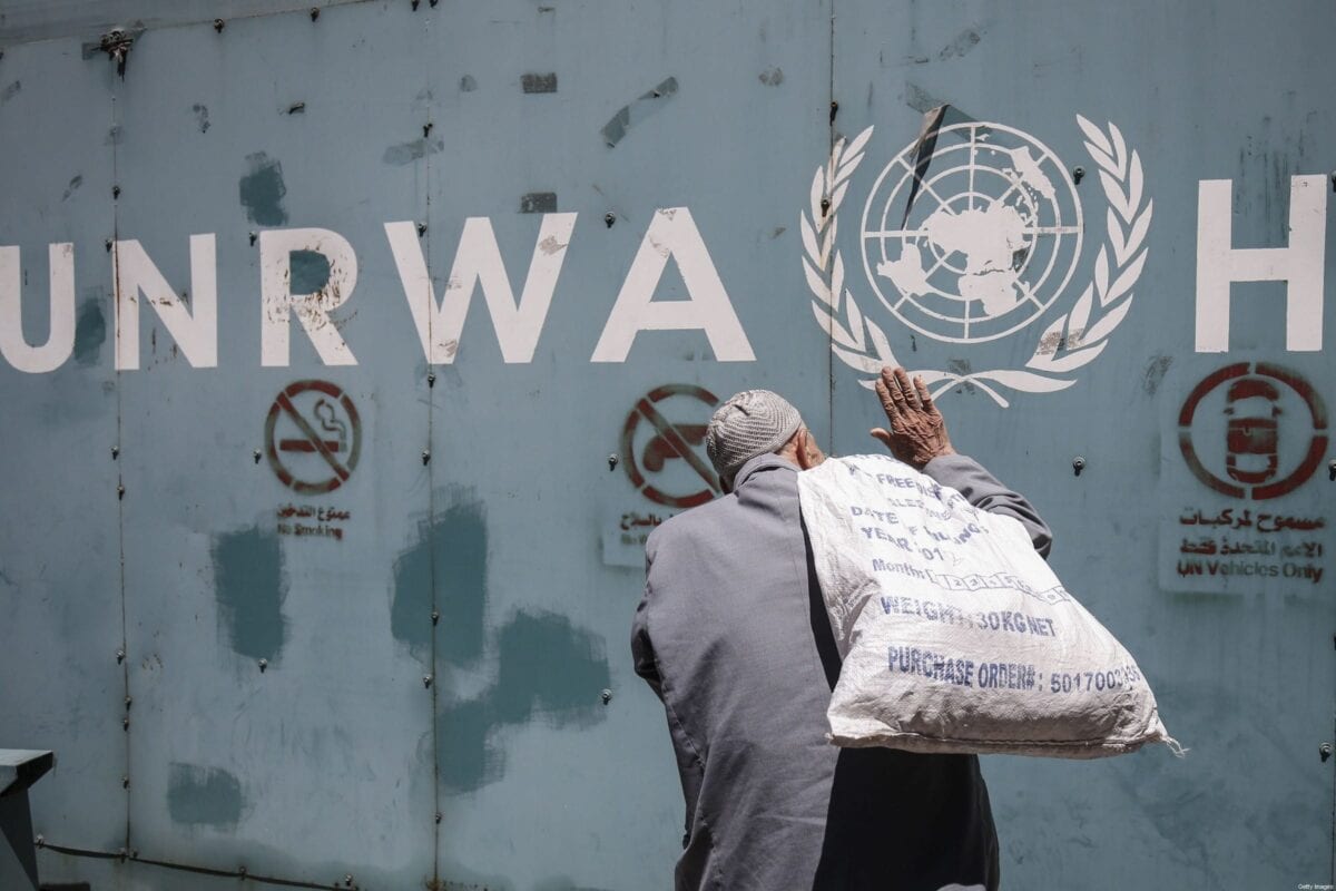 Homem palestino diante do emblema da Agência das Nações Unidas de Assistência aos Refugiados da Palestina no Oriente Próximo (UNRWA), na cidade de Gaza, em 31 de julho de 2018 [SAID KHATIB/AFP/Getty Images]
