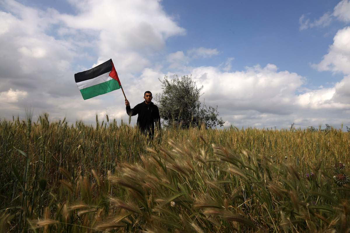 Um homem palestino agita uma bandeira nacional perto da fronteira com Israel, a leste da Cidade de Gaza, em 30 de março de 2021 [Mohammed Abed/AFP via Getty Images]