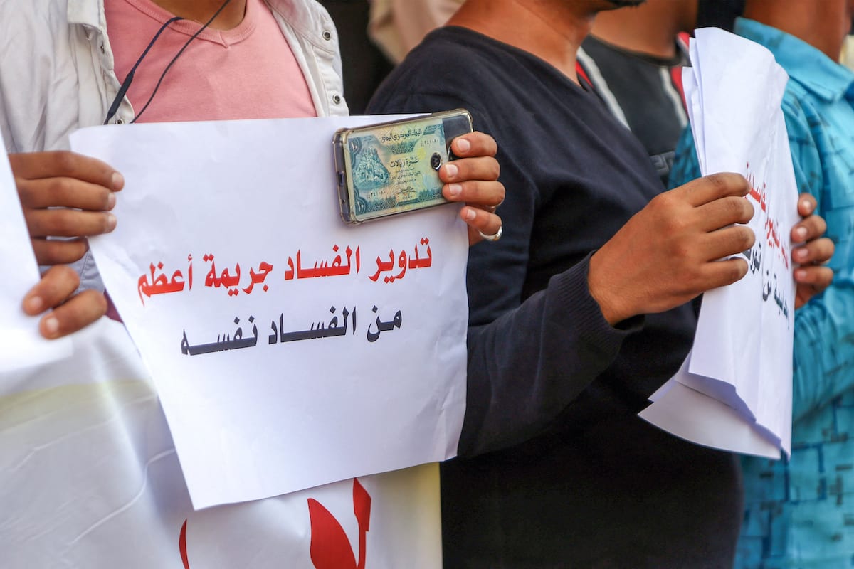 Homem iemenita exibe dinheiro e cartaz em árabe contra a corrupção, durante protesto na cidade de Taez, Iêmen, 3 de junho de 2021 [Ahmad al-Basha/AFP via Getty Images]