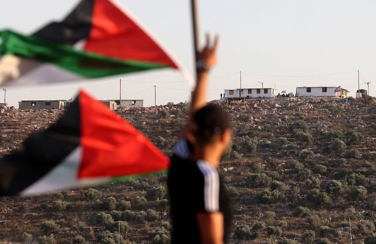Bandeiras palestinas balançam enquanto um jovem faz o sinal da vitória em direção a um novo posto avançado de colonos israelenses na aldeia de Beita, ao sul de Nablus, na Cisjordânia ocupada, em 13 de junho de 2021 [JAAFAR ASHTIYEH/AFP via Getty Images]
