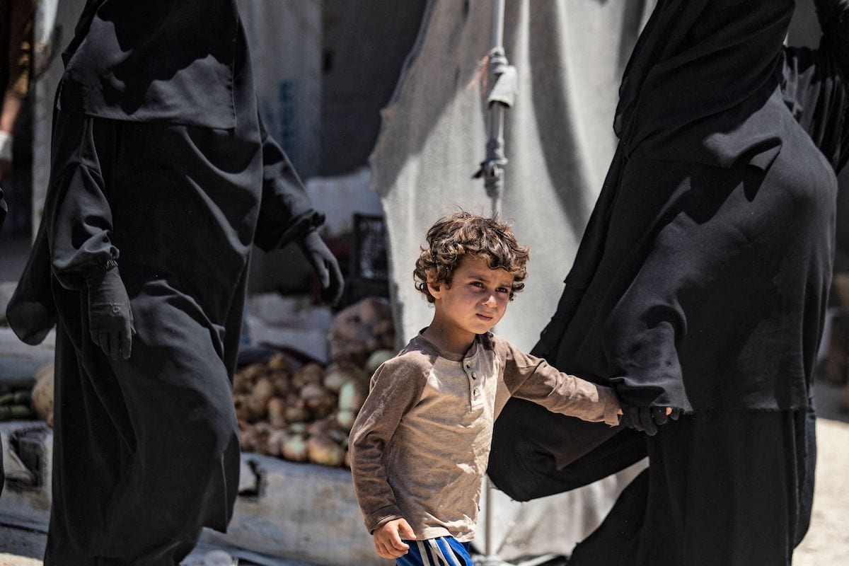 Uma mulher caminha com uma criança no acampamento Kurdish-run al-Hol, que abriga parentes de supostos combatentes do grupo do Daesh, na província de Hasakeh, no nordeste da Síria, em 23 de junho de 2021. [DELIL SOULEIMAN/AFP via Getty Images]