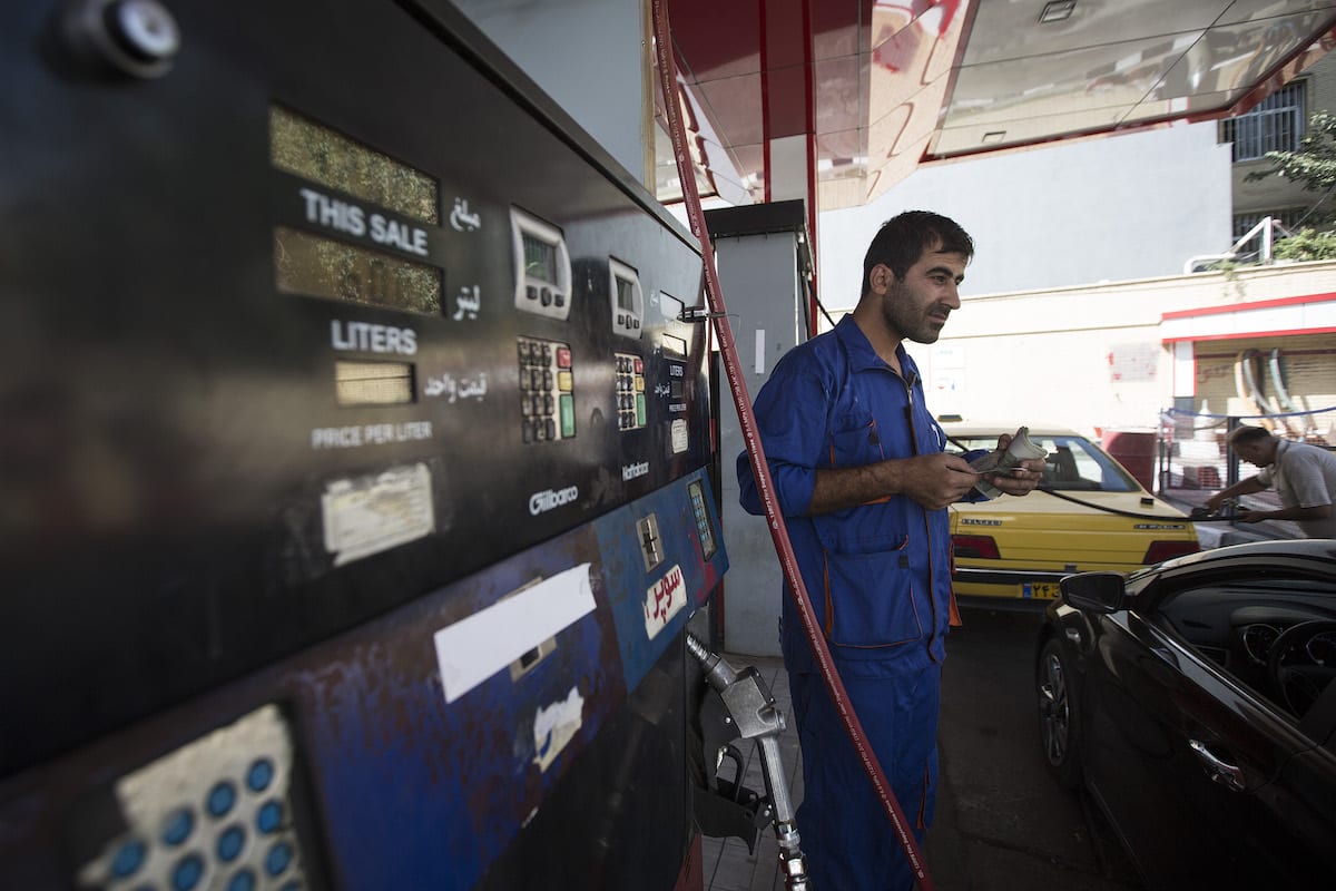 Um frentista segura um maço de notas de Rial enquanto atende clientes em um posto de gasolina operado pela National Iranian Oil Co em Teerã, Irã, em 24 de agosto de 2015 [Simon Dawson/Bloomberg via Getty Images]
