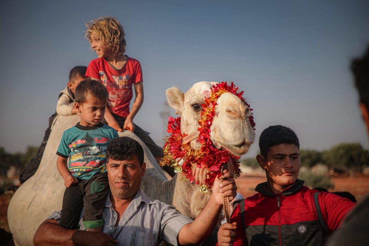 Crianças sírias escalam em um camelo em um acampamento durante o Eid al-Adha em Idlib, Síria, em 20 de julho de 2021. Os sírios foram forçados a deixar suas casas devido aos ataques do regime de Assad [Muhammed Said/Agência Anadolu]
