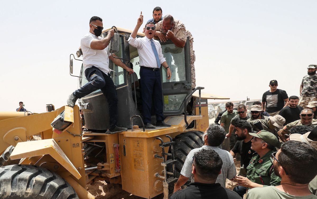 Abdulhamid Dbeibah, primeiro-ministro interino líbio, acena no topo de uma escavadeira em 20 de junho de 2021, na cidade de Buwairat al-Hassoun, durante uma cerimônia para marcar a reabertura de uma estrada de 300 km entre as cidades de Misrata e Sirte. [MAHMUD TURKIA/AFP via Getty Images]
