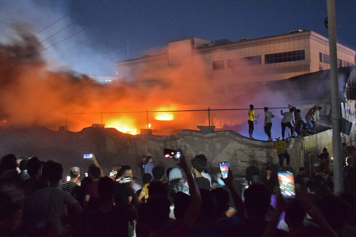 As pessoas se reúnem enquanto um incêndio massivo engendra a ala de isolamento de coronavírus do hospital Al-Hussein no sul do Iraque, na cidade de Nasiriyah, no final de 12 de julho de 2021 [ASAAD NIAZI/AFP via Getty Images].
