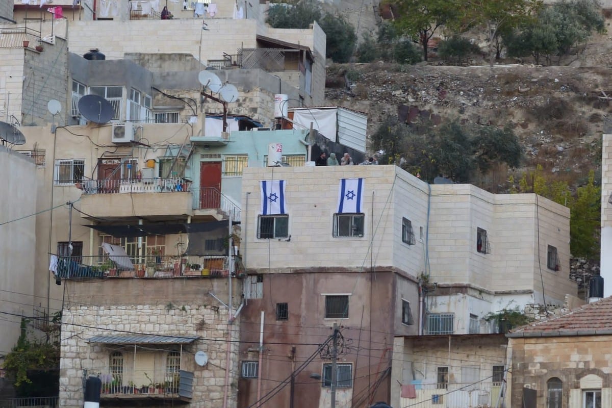 Colonos israelenses hasteiam a bandeira israelense sobre um edifício residencial palestino em Silwan, Jerusalém Oriental ocupada, 2 de julho de 2021

