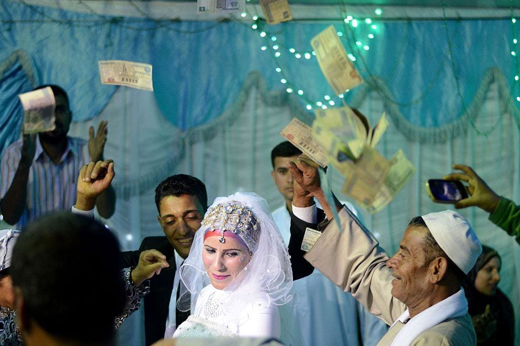 Uma noiva e um noivo recebem uma chuva de dinheiro enquanto dançam durante um casamento na província egípcia do delta do Nilo de al-Minufiyah, em 20 de maio de 2016 [Mohamed El-Shahed/AFP/Getty Images)
