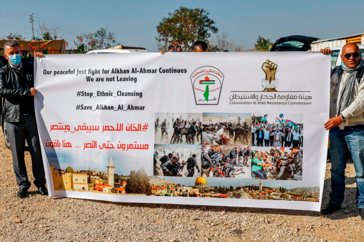 Homens seguram uma placa condenando a ocupação israelense na vila de Khan al-Ahmar na Cisjordânia ocupada por Israel, em 29 de novembro de 2020 [Ahmad Gharabli/AFP via Getty Images]
