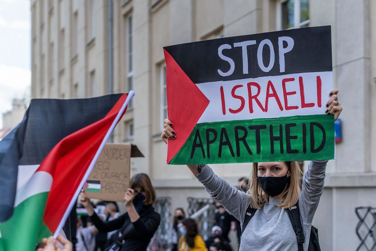 Uma participante segura uma placa dizendo "Pare o Apartheid Israelense" durante um protesto em solidariedade aos palestinos convocados sobre o conflito em curso com Israel em frente à embaixada israelense em Varsóvia, 15 de maio de 2021 [Wojtek Radwanski/AFP via Getty Images]
