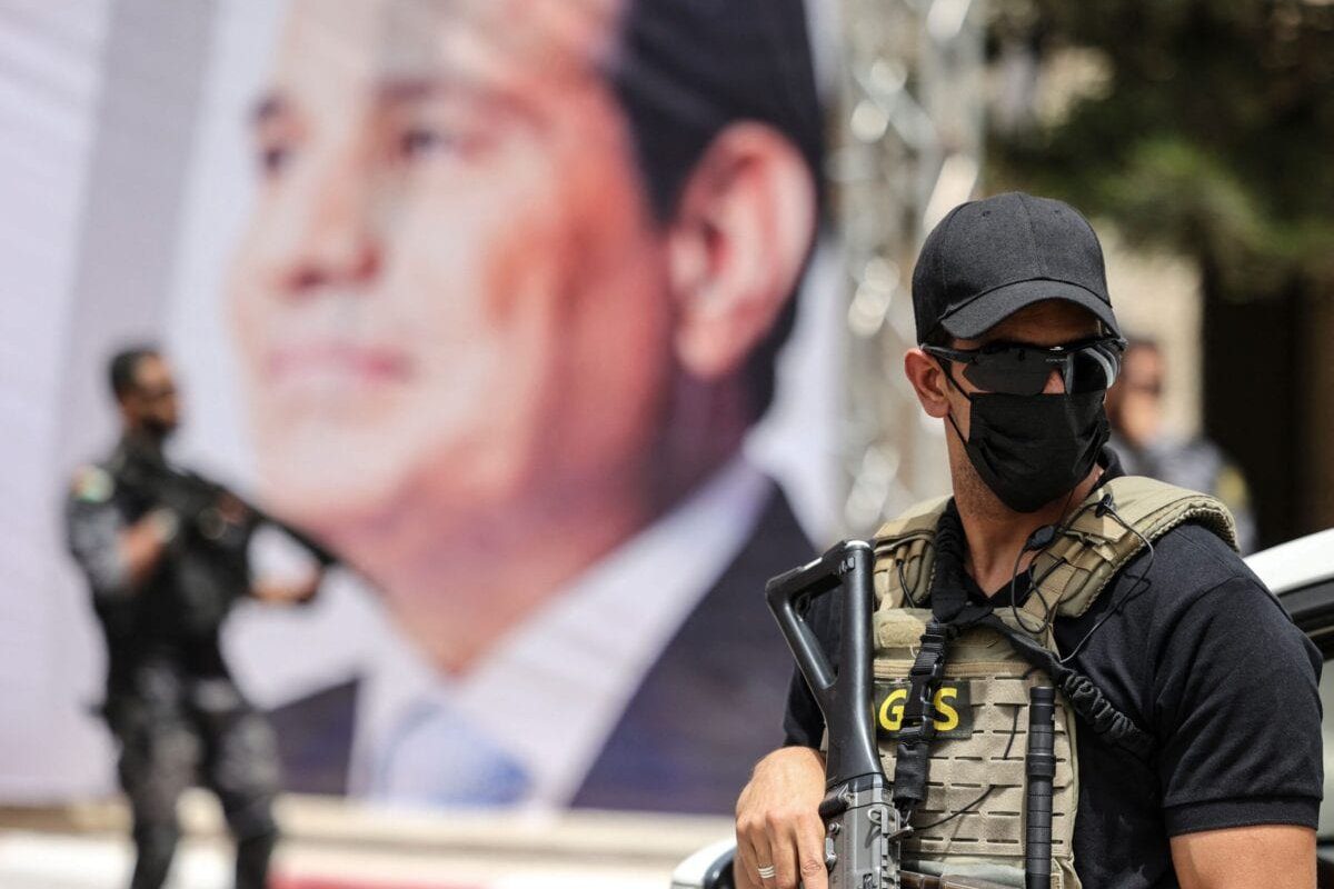 Um membro da segurança da inteligência egípcia fica de guarda perto de um banner mostrando o presidente Abdel Fattah Al-Sisi, em 31 de maio de 2021 [Mahmud Hams/AFP via Getty Images]
